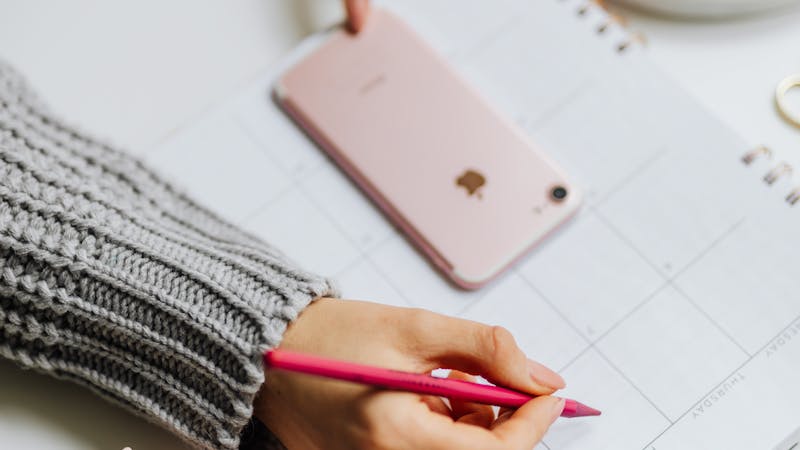 Hand writing on a calendar planner next to a phone.